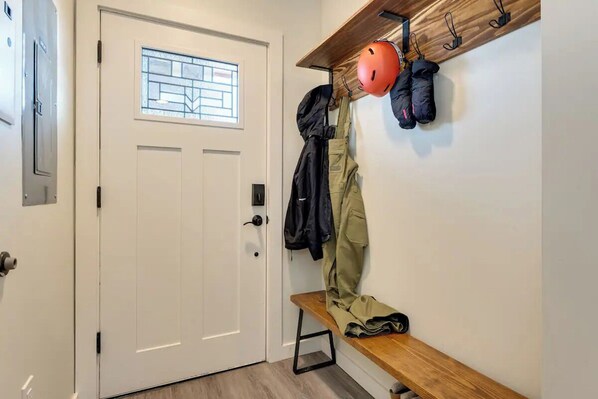A door with a window, a bench, and a wall-mounted rack with helmets and jackets.