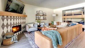 A cozy living room with a fireplace, sofa, TV, and bunk beds. - Government Camp Condo: Ski-in/Ski-out, Mountain Views, Walk to Downtown (Government Camp)