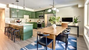 A modern kitchen with green cabinets, a wooden island, bar stools, and a dining table with chairs. - Government Camp Condo: Ski-in/Ski-out, Mountain Views, Walk to Downtown (Government Camp)