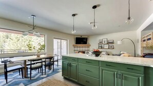 A modern kitchen with green cabinets, a large island, pendant lights, and a dining area with a blue rug. - Government Camp Condo: Ski-in/Ski-out, Mountain Views, Walk to Downtown (Government Camp)