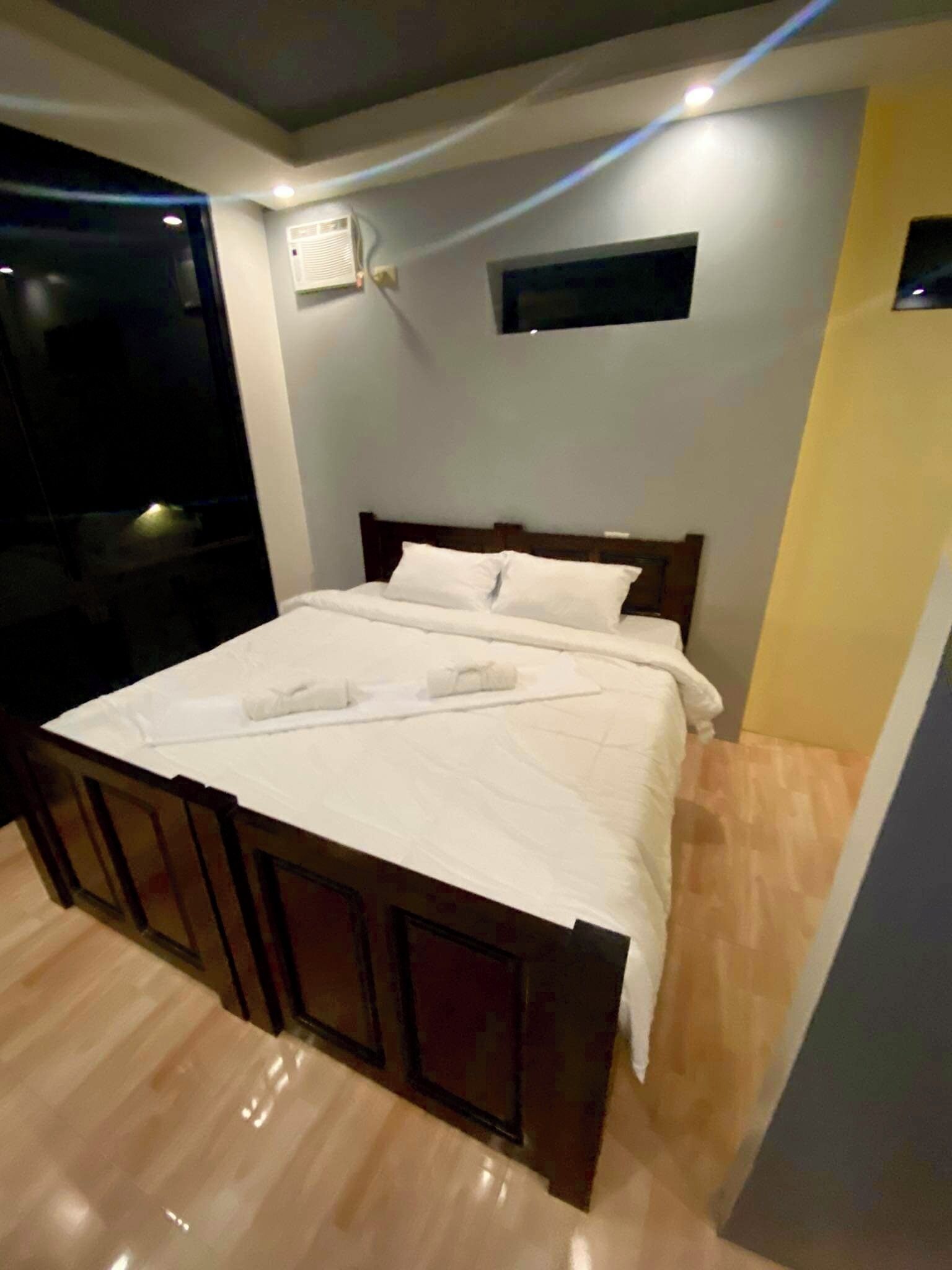 Un lit bien fait, avec du linge de lit blanc, dans une pièce au plancher en bois et dotée d’une petite fenêtre.