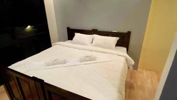 Un lit bien fait, avec du linge de lit blanc, dans une pièce au plancher en bois et dotée d’une petite fenêtre.