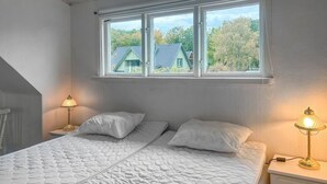 A bedroom with a bed, two bedside lamps, and a window overlooking a house and trees. - Stunning home in Sölvesborg with house sea view (Sölvesborg)