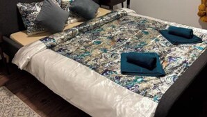 A neatly made bed with patterned bedding, a bedside lamp, and a floor lamp. - Mirvana Apartments Metheor Executive Suite (Timișoara)