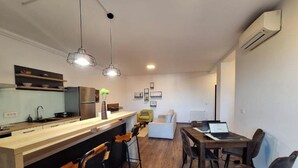 A modern kitchen with a wooden countertop, bar stools, and pendant lighting. There is a dining area with a wooden table and chairs. - Mirvana Apartments Metheor Executive Suite (Timișoara)