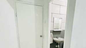 Un pasillo estrecho con una puerta blanca que da a un baño con lavamanos y espejo.