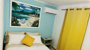 Un dormitorio con una cama, una mesita de noche, un equipo de aire acondicionado y un cuadro de una playa.