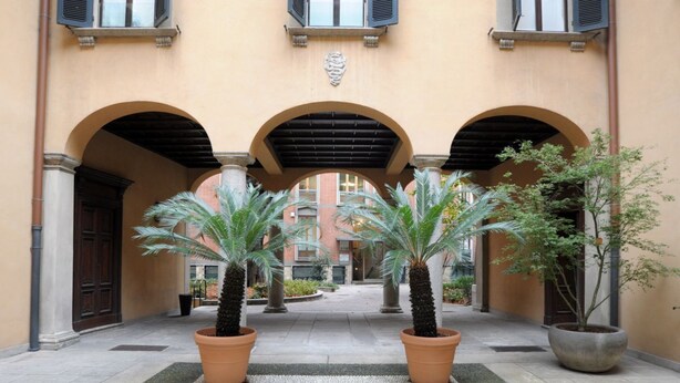 A courtyard with three arches, potted palm trees, and a building facade with a stone crest.