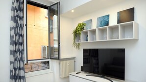 A modern living room with a large flat-screen TV, white cabinetry, a potted plant, and artwork on the wall.