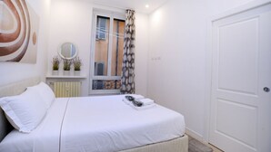 A bedroom with a bed, a window with blinds, a door, and a wall-mounted mirror.
