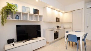 A modern kitchen with white cabinetry, a built-in oven, and a dining area with a white table and blue chairs.
