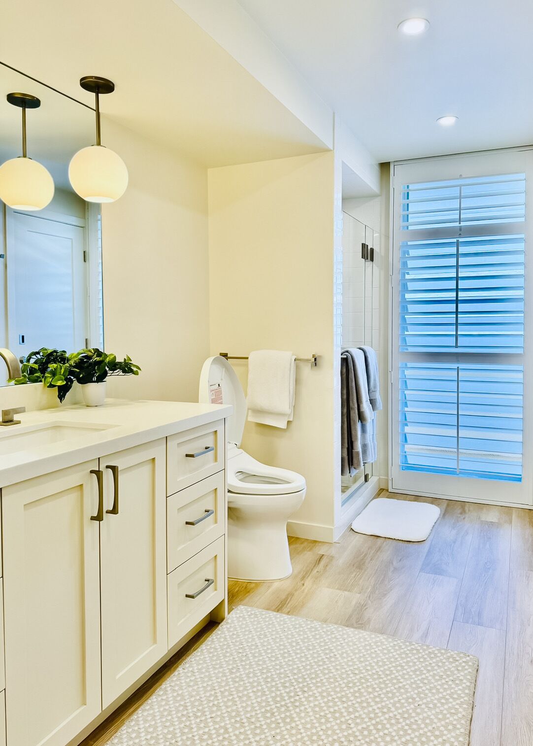 Een moderne badkamer met toilet, wastafel en spiegel. Boven de wastafel hangen twee lampen en op het aanrecht staat een potplant.