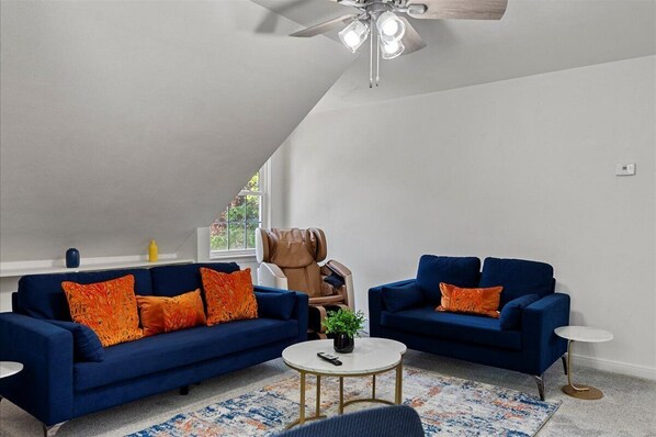 A modern living room with two blue sofas, a ceiling fan, and a small round table.