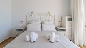 Ein ordentlich bezogenes Bett mit weißen Leinen und Kissen, zwei Nachttische mit Lampen, ein kleiner Schrank und ein Fenster mit Vorhängen.