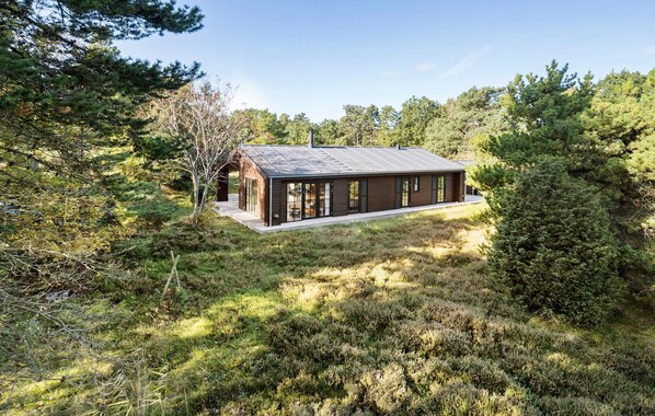 A modern cabin with a sloped roof, surrounded by dense forest.