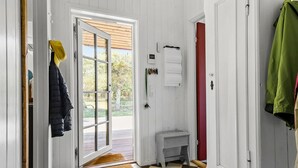 Um quarto com porta de madeira, um pequeno banco branco, uma porta vermelha e um casaco verde pendurado na parede.