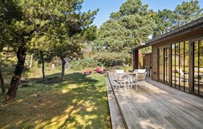 A wooden deck with outdoor furniture, surrounded by trees and a clear sky.