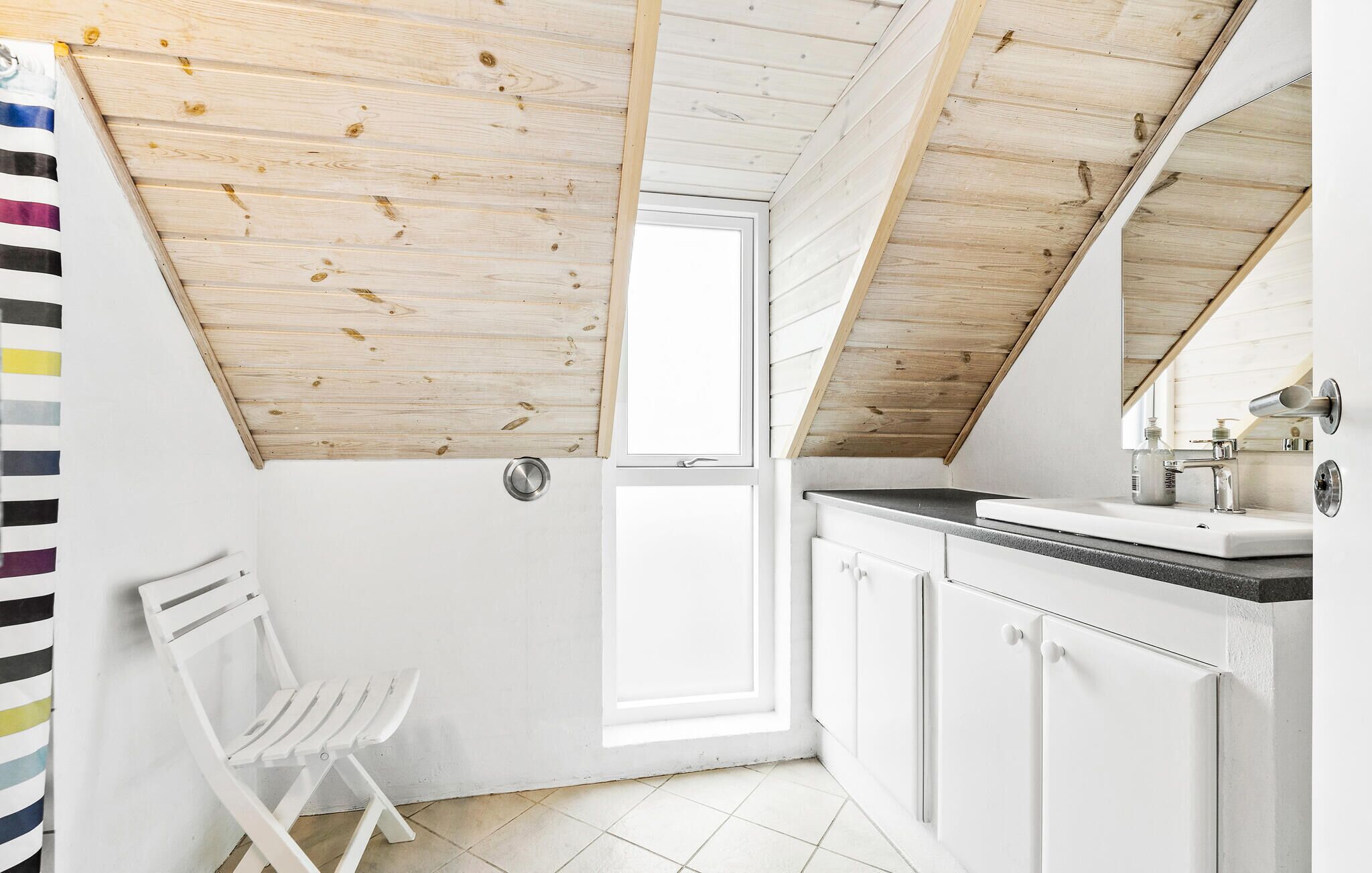 Une petite salle de bain de style mansardé, aux murs blancs, avec un plafond en bois, un lavabo blanc et un miroir.