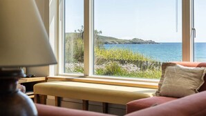 A room with a large window overlooking a coastal landscape, a bench, and a lamp.