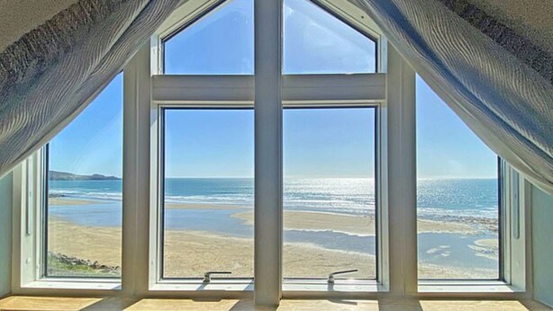 A room with a large bay window overlooking a beach.