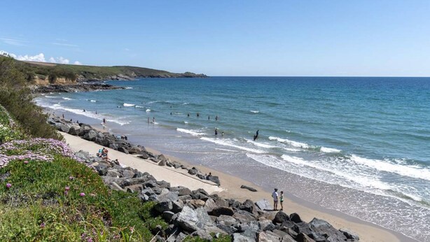 A beach with rocky shoreline, clear blue water, and people swimming and walking along the shore. - Private Cliff top Retreat by Perranuthnoe Beach (Penzance)