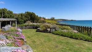 A coastal garden with a wooden fence, a stone wall, and a variety of flowers.