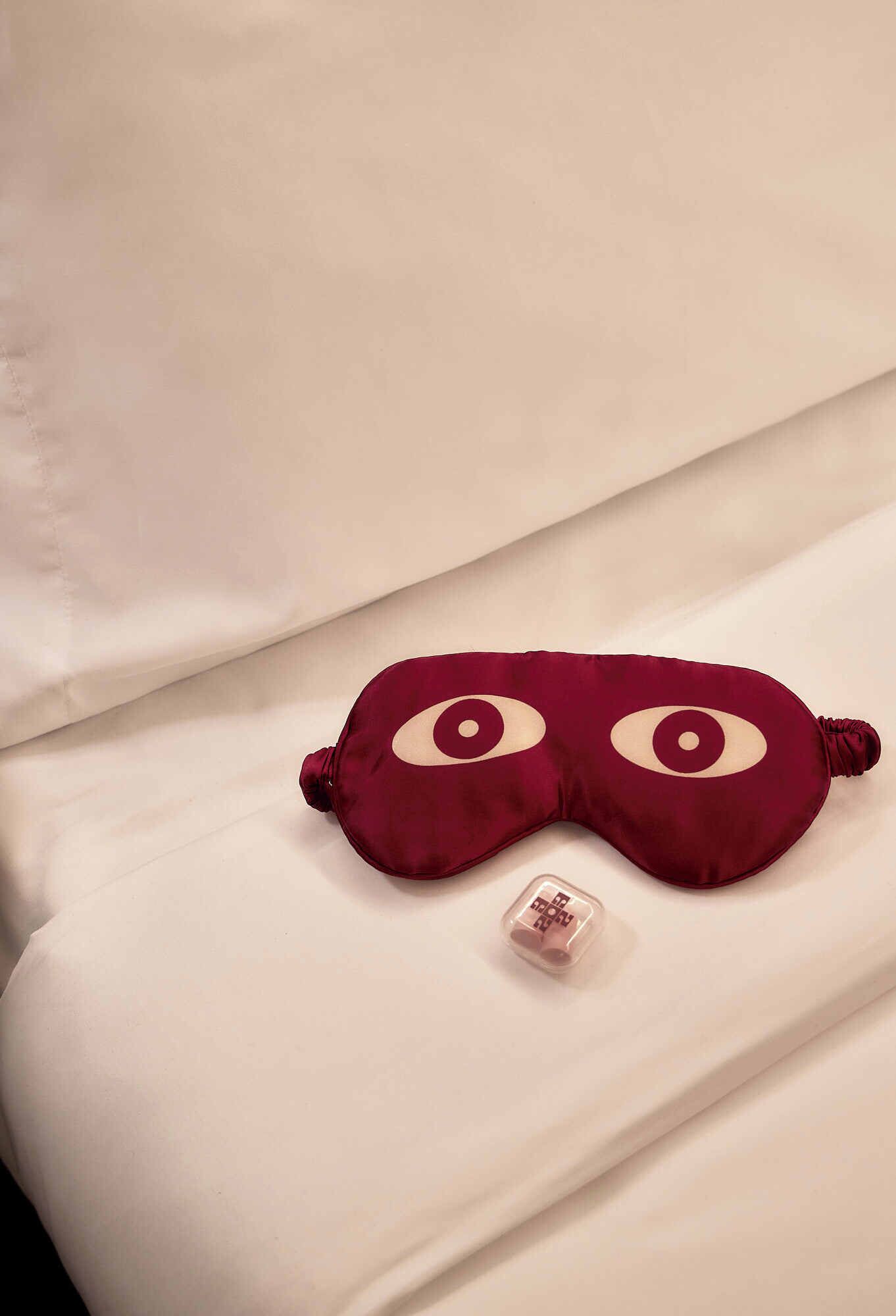 A bed with a red eye-shaped pillow and a small decorative item on it.