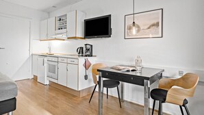 A compact kitchen with a built-in oven, a coffee maker, and a flat-screen TV. There is a dining table with two chairs and a framed picture on the wall. - Awesome apartment in Nexø with WiFi (Nexø)