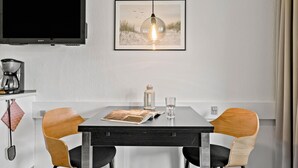A modern dining area with a flat-screen TV, a framed beach scene, a coffee maker, and a table with chairs. - Awesome apartment in Nexø with WiFi (Nexø)