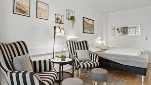 A modern bedroom with a bed, two striped armchairs, a small table, and a floor lamp. There are framed pictures on the wall and a window with a view. - Awesome apartment in Nexø with WiFi (Nexø)