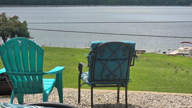 On peut voir un lac, des chaises disposées face à l’eau, une jetée avec un bateau et une zone herbeuse.