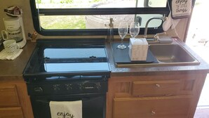 Une cuisine équipée d’une cuisinière, d’un évier et d’une fenêtre. On y trouve deux tasses, une machine à café et une boîte de mouchoirs sur le comptoir.