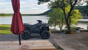Un véhicule tout-terrain est stationné sur une zone de gravier, à proximité d’une terrasse en bois et d’un parasol rouge.