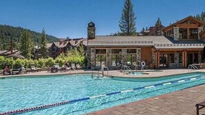 Uma área de piscina com piscina azul cristalina, um edifício de pedra com grandes janelas e montanhas ao fundo.