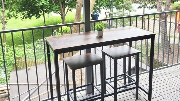 A wooden deck with a table and two chairs, surrounded by a metal railing, overlooking a lush green landscape. - Newly Renovated 2-Bedroom Oasis (Toronto)