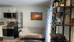 A modern kitchen with stainless steel appliances, a grey sofa, a colorful rug, and a painting on the wall. - Newly Renovated 2-Bedroom Oasis (Toronto)