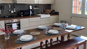 Una cocina moderna con armarios blancos, una mesa de comedor de madera para cuatro personas y un ventanal con vistas al exterior.