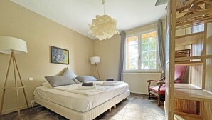 Un dormitorio con cama, una lámpara de pie, un cuadro, una ventana con cortinas y una silla de madera.