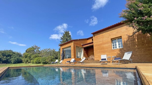 Una casa de madera con piscina y sillones de descanso.