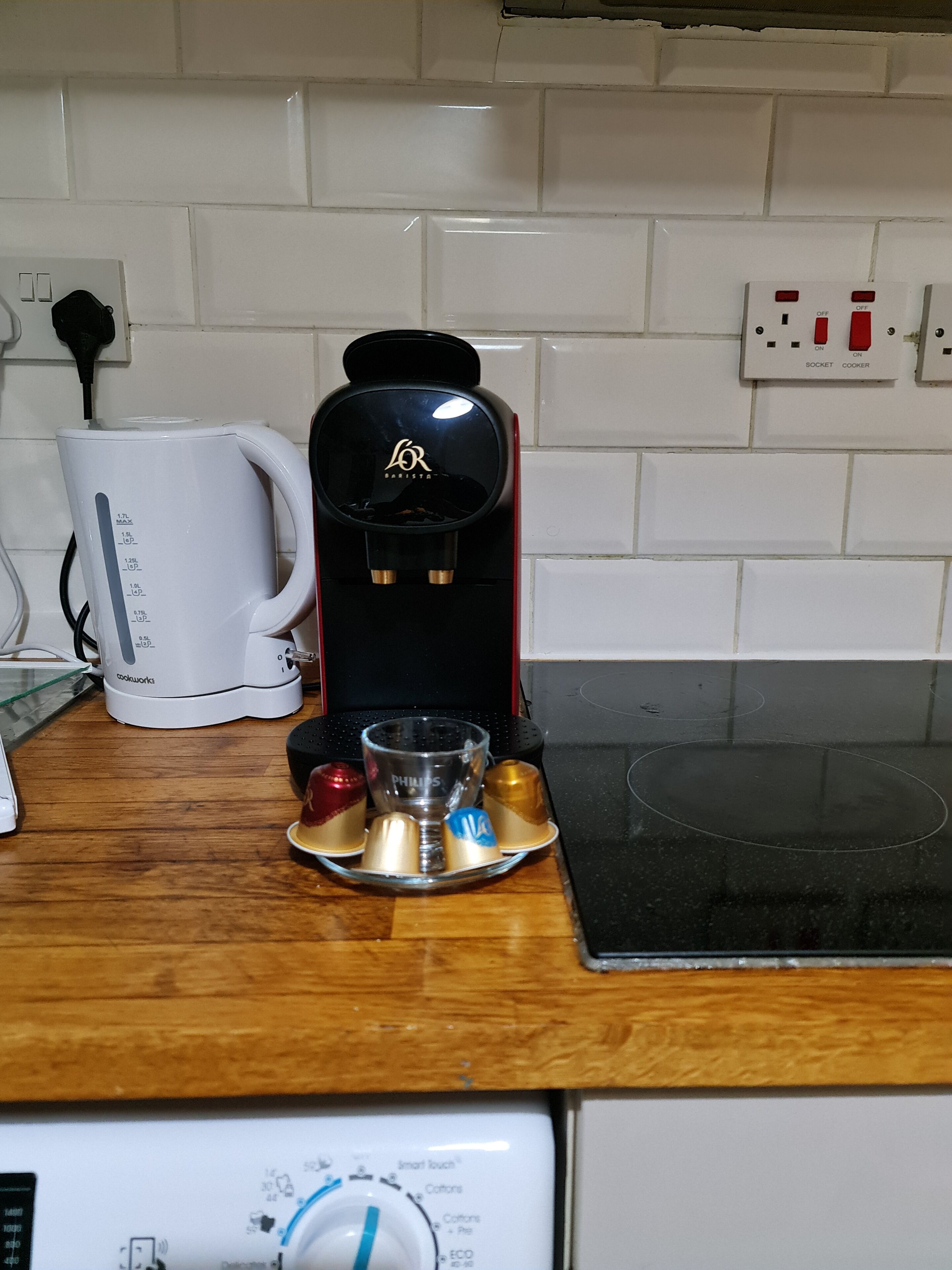 A coffee maker on a kitchen counter with a white mug, a glass carafe, and a tray with coffee cups.