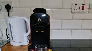 A coffee maker on a kitchen counter with a white mug, a glass carafe, and a tray with coffee cups. - Stylish studio- 15mins to Central London! (London)