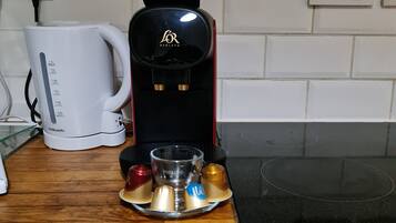 A coffee maker on a kitchen counter with a white mug, a glass carafe, and a tray with coffee cups.