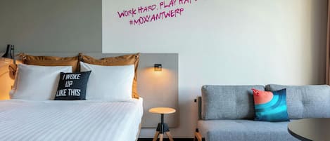 A hotel room with a bed, a sofa, a small table, and a wall with motivational text.