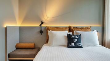A hotel room with a bed, a bedside table, a wall-mounted lamp, and a pillow with text.