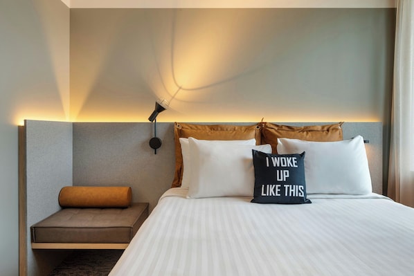 A hotel room with a bed, a bedside table, a wall-mounted lamp, and a pillow with text. - Moxy Antwerp (Antwerp)