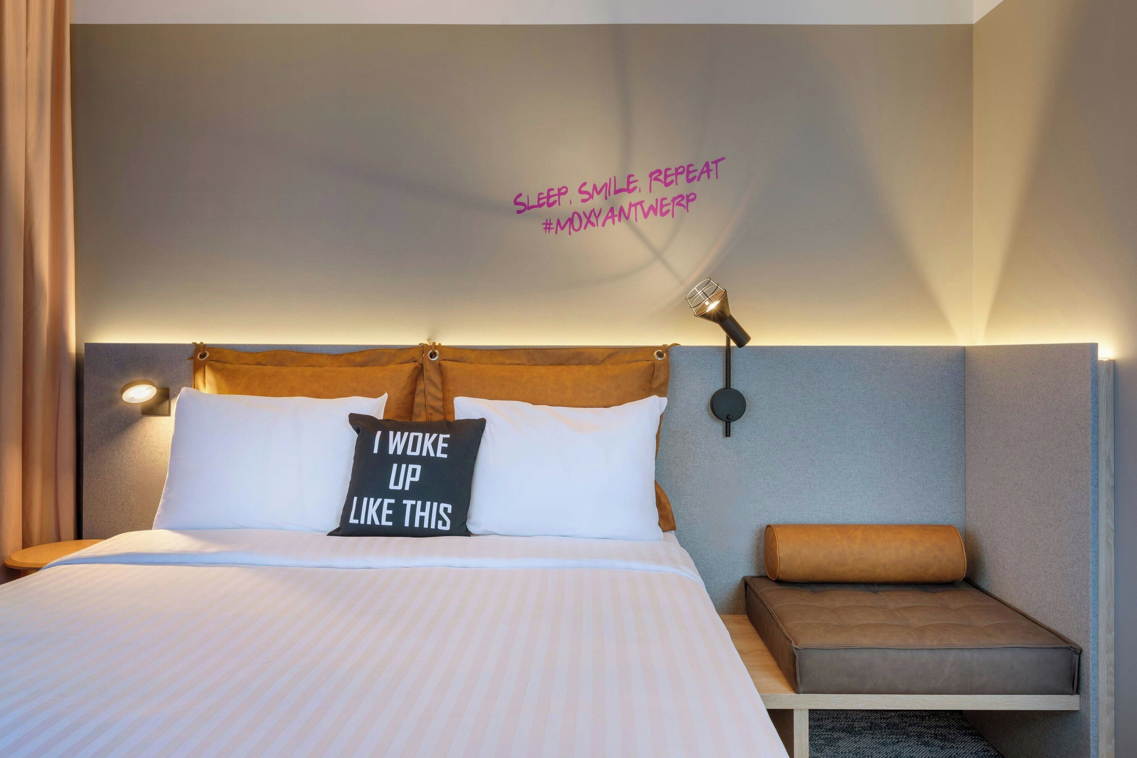 Een net opgemaakt bed met een kussen waarop staat: 'Zo ben ik wakker geworden'.
