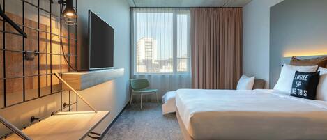 Una habitación de hotel con una cama, televisor, una silla y un ventanal con cortinas.