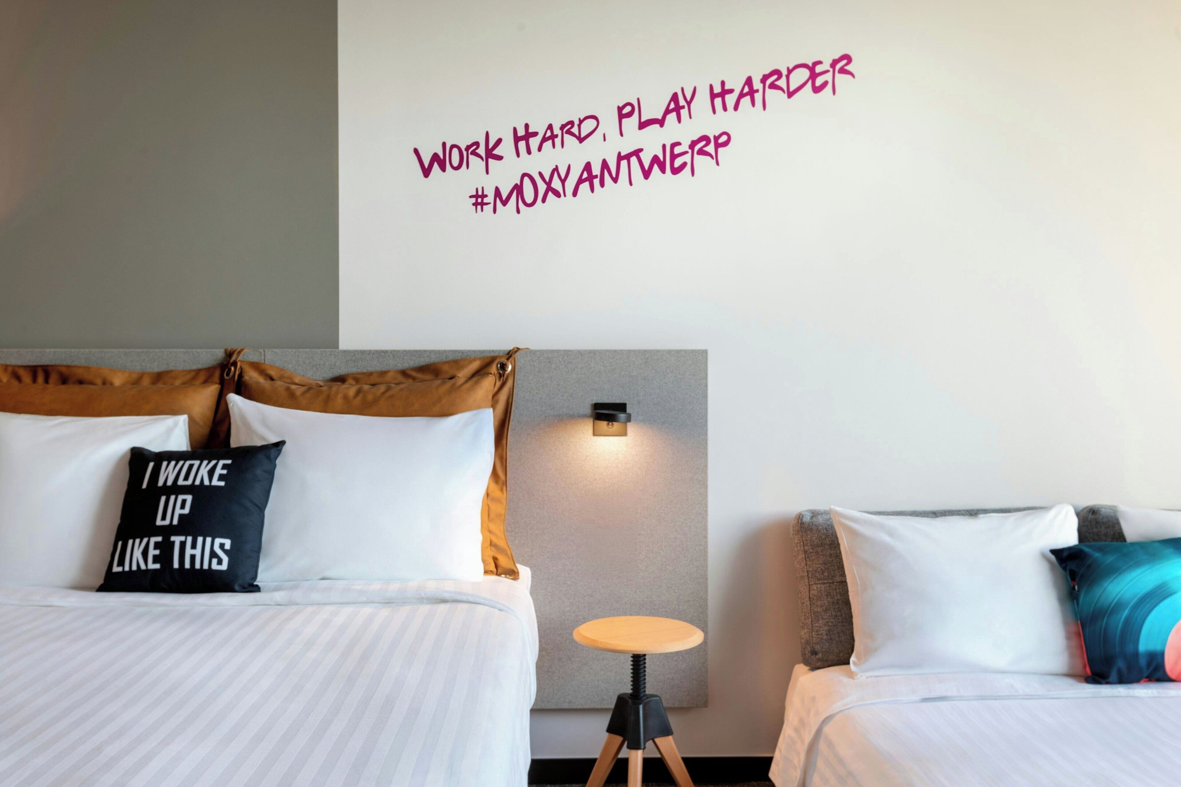 Habitación de hotel con dos camas, una lámpara de pared y una frase motivadora.