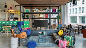 A modern living room with a large TV, comfortable seating, and a bookshelf filled with decorative items. - Moxy Antwerp (Antwerp)