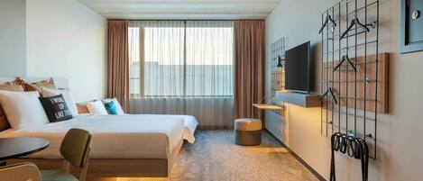 A hotel room with a bed, a desk, a chair, a TV, and a coat rack.